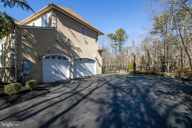 view of property exterior featuring an attached garage, fence, driveway, and stucco siding