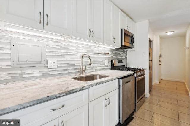 kitchen featuring light stone countertops, a sink, appliances with stainless steel finishes, white cabinetry, and backsplash