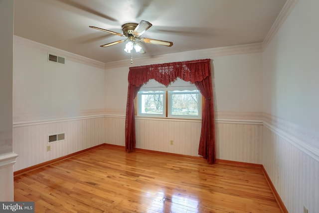 unfurnished room with visible vents, wainscoting, light wood-style flooring, and ceiling fan