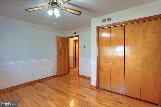 unfurnished bedroom featuring visible vents, a wainscoted wall, a closet, crown molding, and light wood finished floors