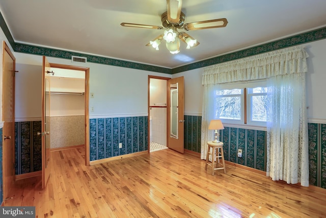 empty room with visible vents, wallpapered walls, wainscoting, hardwood / wood-style flooring, and a ceiling fan