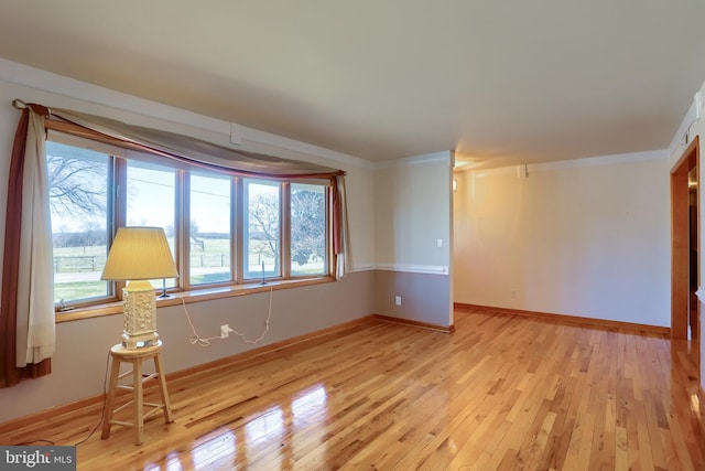 unfurnished room with plenty of natural light, light wood-style flooring, baseboards, and ornamental molding