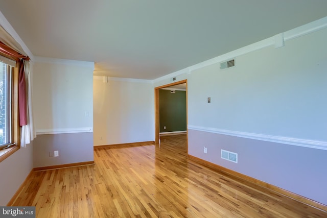 spare room featuring visible vents, baseboards, light wood-style floors, and crown molding