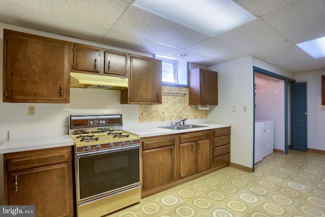 kitchen featuring washing machine and clothes dryer, range with gas cooktop, under cabinet range hood, light countertops, and a sink