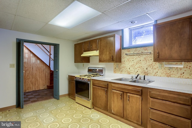 kitchen with light countertops, white gas stove, under cabinet range hood, and a sink