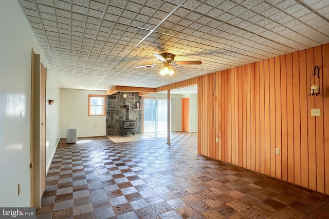 unfurnished living room featuring wooden walls, a wood stove, and a ceiling fan