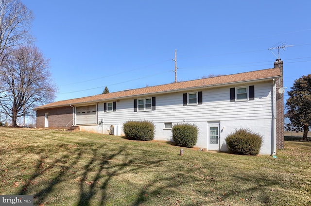 rear view of property with entry steps, an attached garage, a lawn, and a chimney