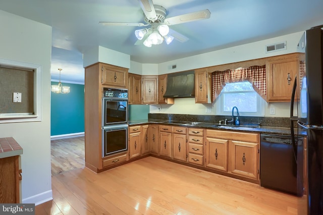 kitchen featuring visible vents, a sink, black appliances, exhaust hood, and light wood-type flooring