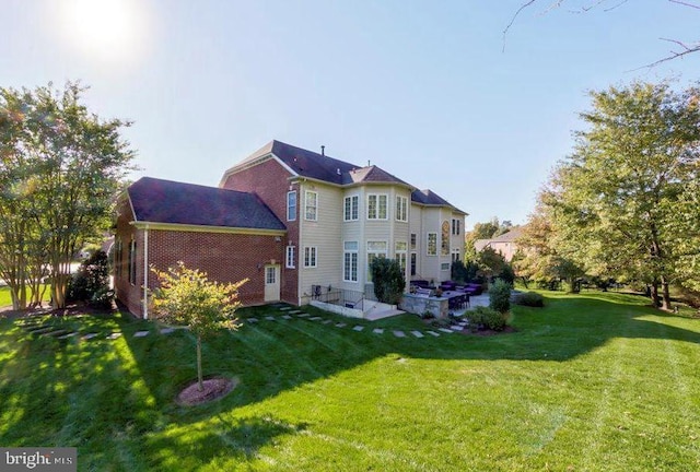 back of property with a patio, a lawn, and brick siding