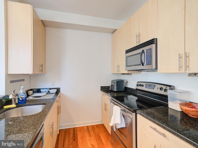 kitchen with light brown cabinetry, appliances with stainless steel finishes, dark stone counters, and a sink