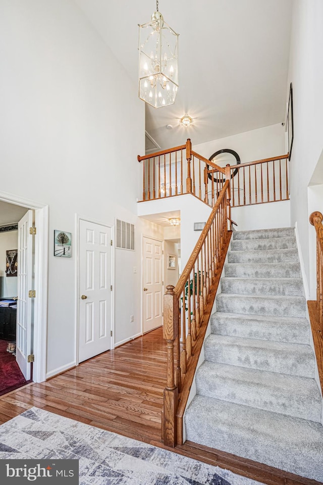 stairs featuring an inviting chandelier, wood finished floors, visible vents, and baseboards