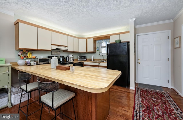 kitchen with black appliances, butcher block counters, a peninsula, white cabinetry, and a sink