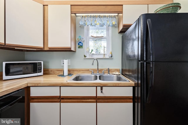 kitchen featuring a sink, butcher block countertops, black appliances, and white cabinets