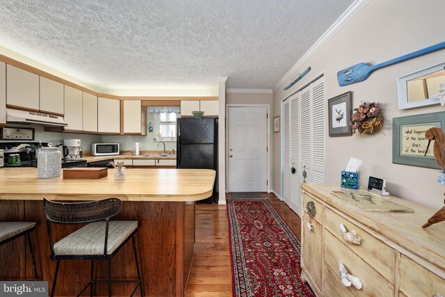 kitchen with under cabinet range hood, butcher block countertops, a kitchen bar, a peninsula, and dark wood-style floors