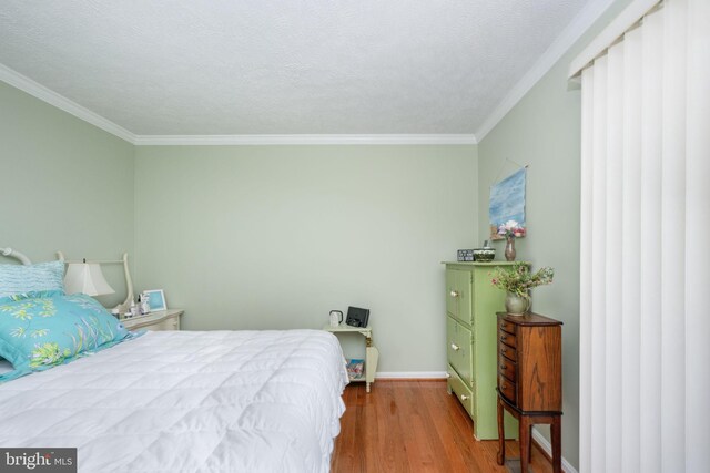 bedroom featuring baseboards, a textured ceiling, wood finished floors, and ornamental molding