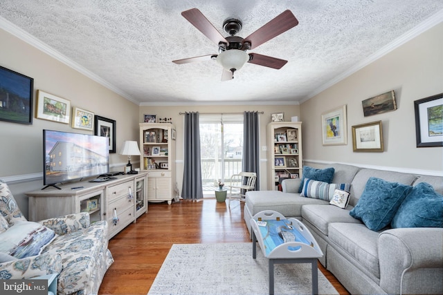 living area with ceiling fan, a textured ceiling, wood finished floors, and crown molding