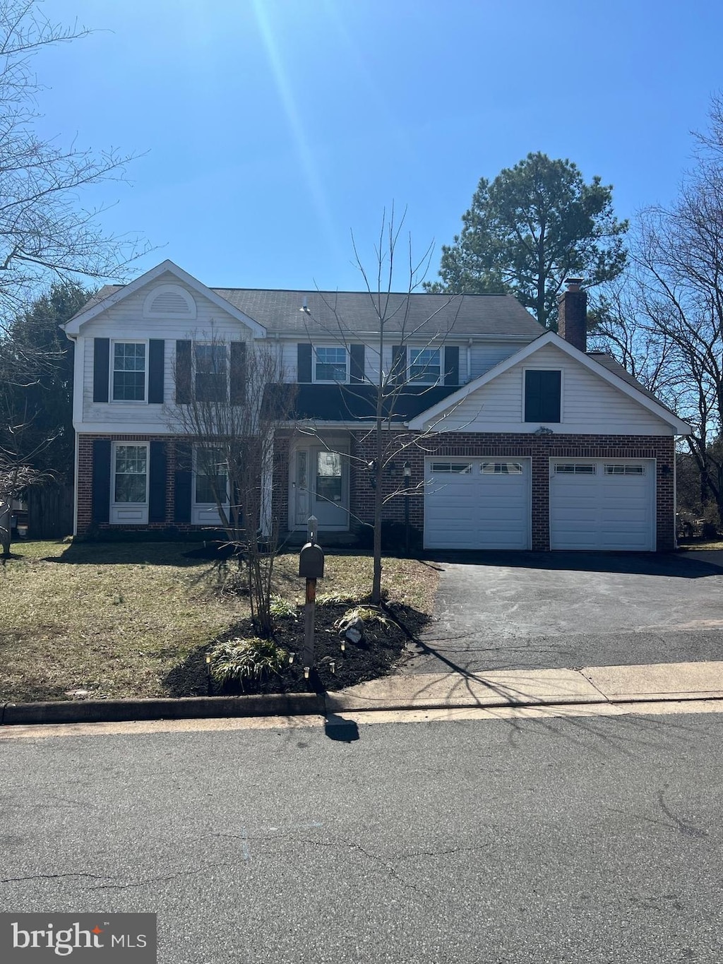 view of front facade featuring brick siding, a chimney, aphalt driveway, and a garage