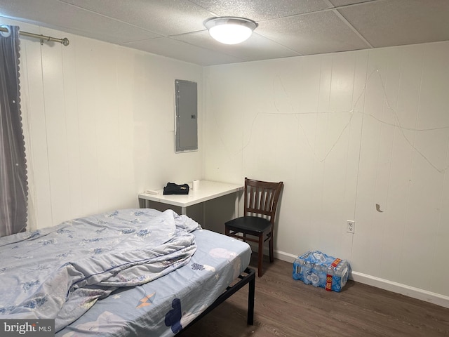 bedroom featuring electric panel, a drop ceiling, baseboards, and wood finished floors