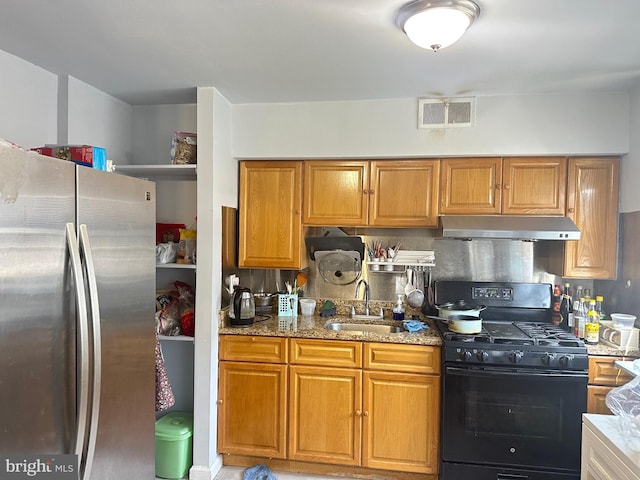 kitchen with visible vents, under cabinet range hood, a sink, black gas stove, and freestanding refrigerator