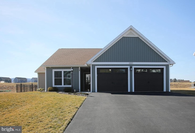 view of front facade with fence, aphalt driveway, roof with shingles, a front yard, and an attached garage