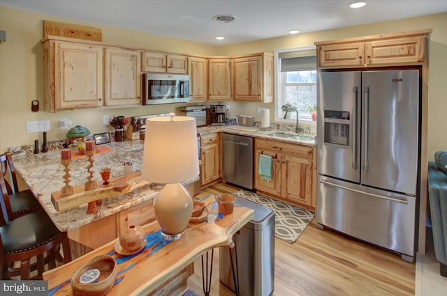 kitchen with light brown cabinets, visible vents, a sink, stainless steel appliances, and light wood-style floors