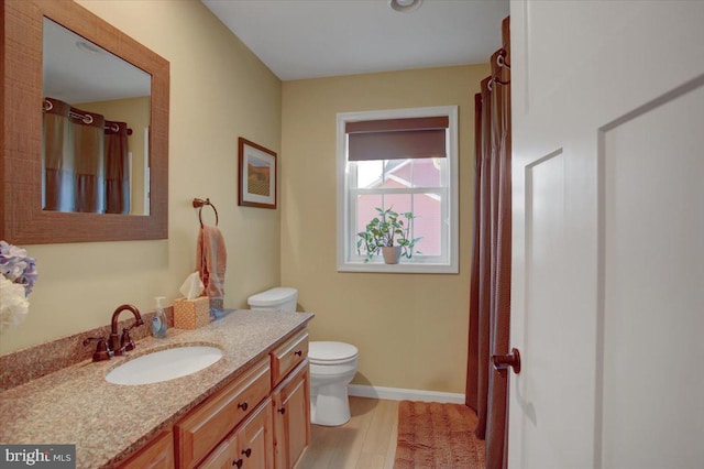 bathroom with baseboards, toilet, wood finished floors, and vanity