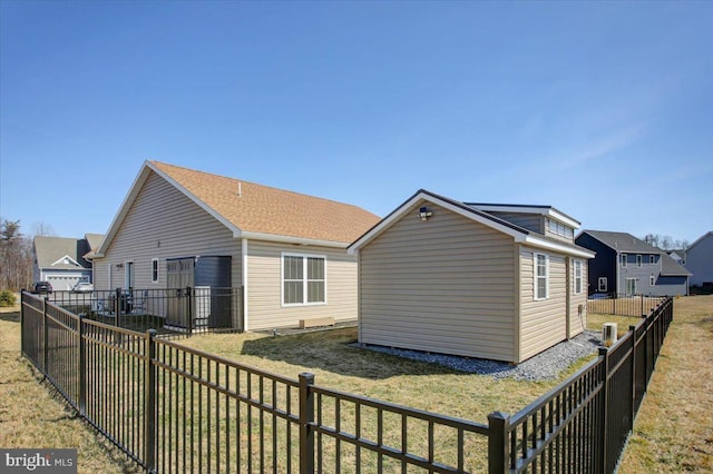 rear view of property with a yard, a fenced backyard, an outdoor structure, and a shingled roof