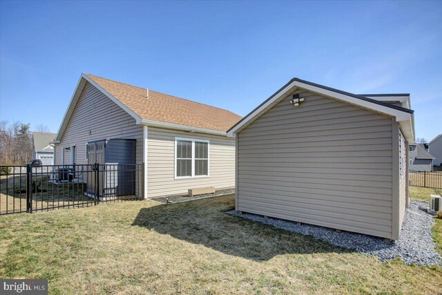 view of home's exterior featuring a shingled roof, fence, a lawn, a storage shed, and an outbuilding