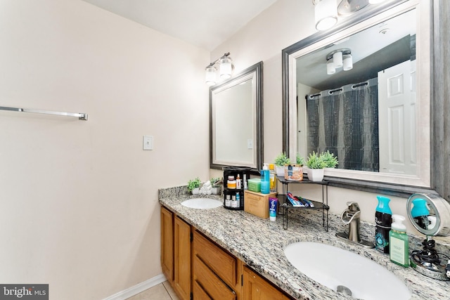 full bath with tile patterned floors, double vanity, baseboards, and a sink