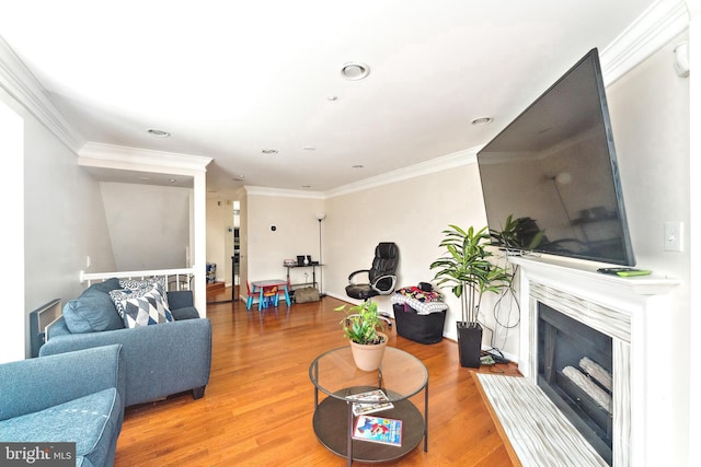 living room with a fireplace with raised hearth, light wood-style flooring, and ornamental molding