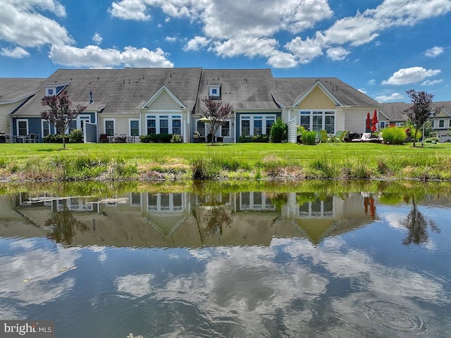 back of property with a water view and a lawn