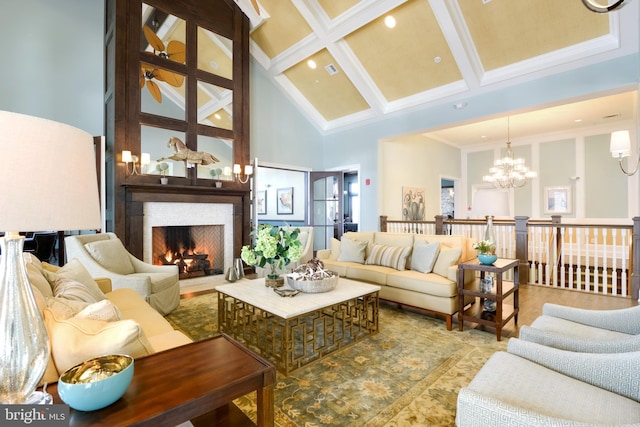 living area with beam ceiling, a notable chandelier, coffered ceiling, a warm lit fireplace, and a towering ceiling