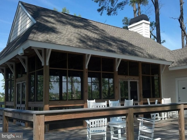 exterior space featuring a deck, a chimney, a sunroom, and a shingled roof