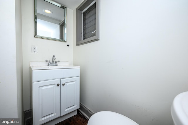 half bath featuring baseboards, toilet, wood finished floors, and vanity