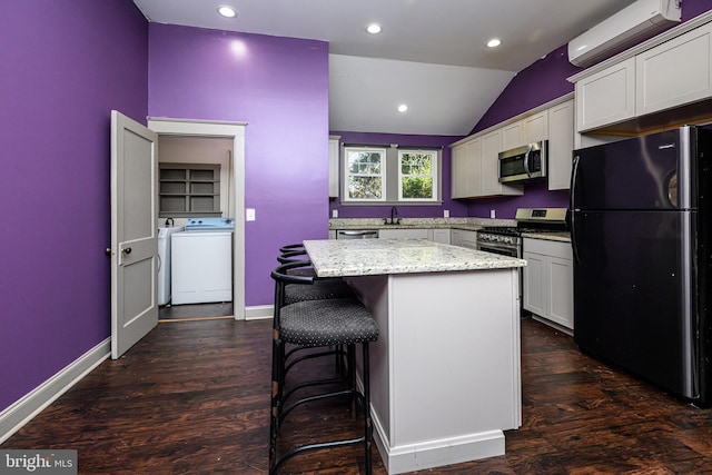 kitchen with a kitchen island, an AC wall unit, vaulted ceiling, appliances with stainless steel finishes, and washer and dryer