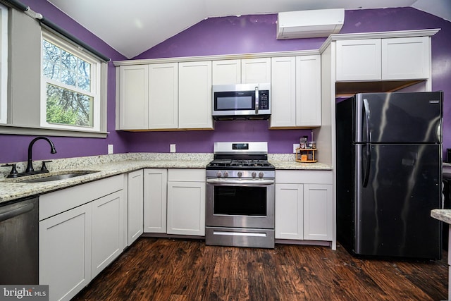 kitchen with dark wood-type flooring, an AC wall unit, lofted ceiling, stainless steel appliances, and a sink