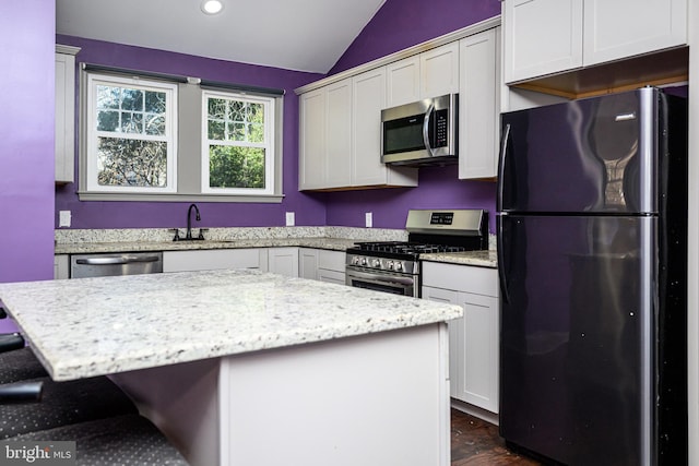 kitchen with light stone countertops, a kitchen bar, lofted ceiling, stainless steel appliances, and a sink