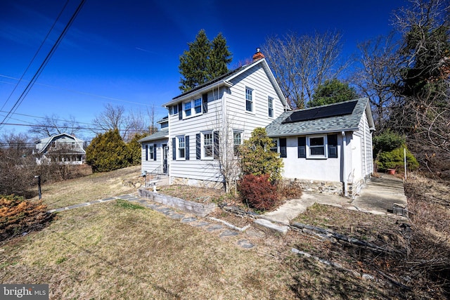 view of front facade with a front lawn, solar panels, a chimney, and roof with shingles