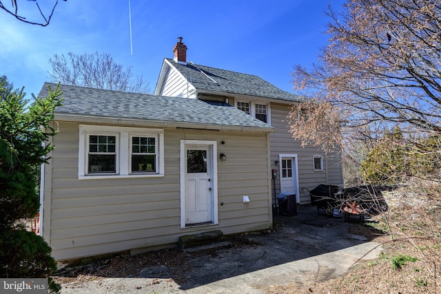 rear view of property with a chimney and roof with shingles