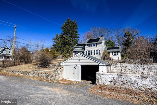 exterior space featuring solar panels, a detached garage, fence, and an outbuilding