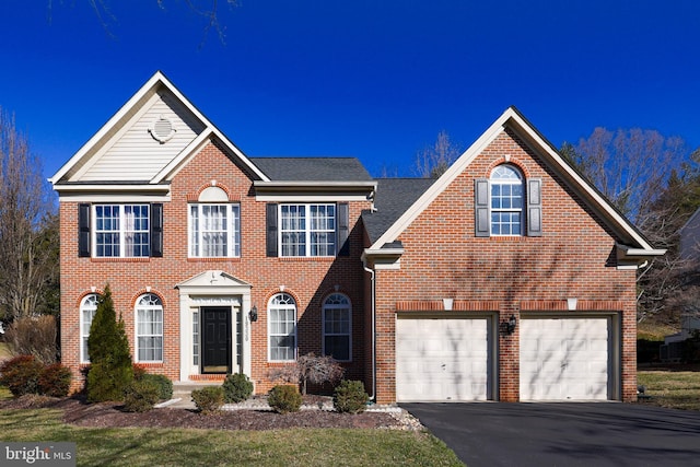 colonial-style house with aphalt driveway, a garage, brick siding, and a shingled roof