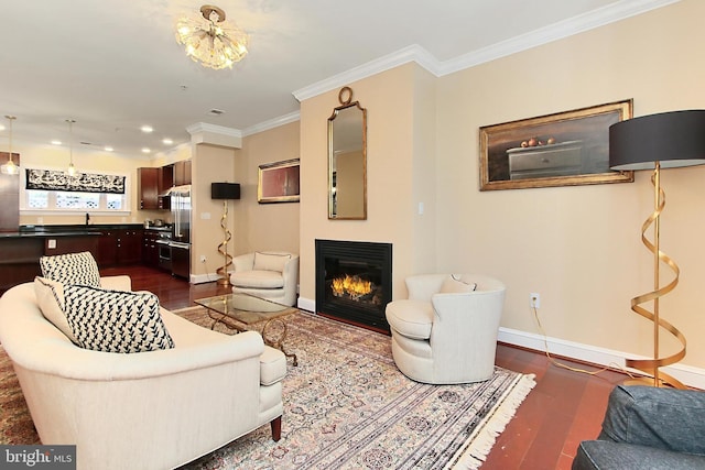 living area featuring a glass covered fireplace, dark wood finished floors, an inviting chandelier, crown molding, and baseboards