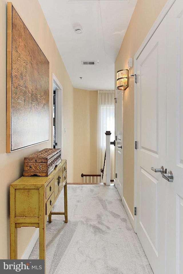 hall with baseboards, an upstairs landing, visible vents, and light carpet