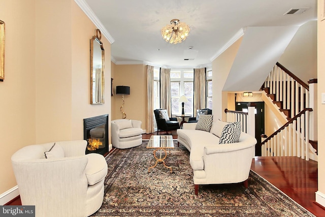 living area featuring visible vents, a baseboard heating unit, a glass covered fireplace, wood finished floors, and crown molding