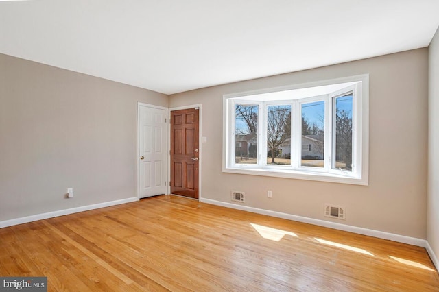 empty room featuring visible vents, light wood-type flooring, and baseboards