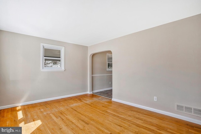 spare room featuring light wood-style floors, arched walkways, visible vents, and baseboards