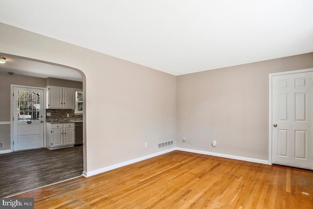 unfurnished living room featuring light wood-style flooring, arched walkways, visible vents, and baseboards