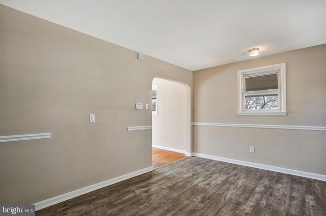 unfurnished room with wood finished floors, baseboards, and arched walkways