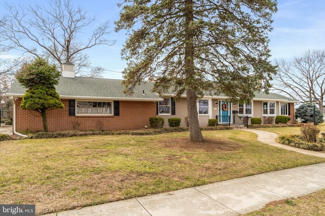 single story home with brick siding, a chimney, a front yard, and roof with shingles