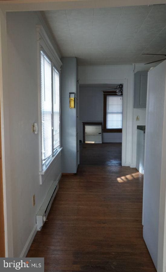 corridor with dark wood-type flooring, baseboards, and a baseboard radiator